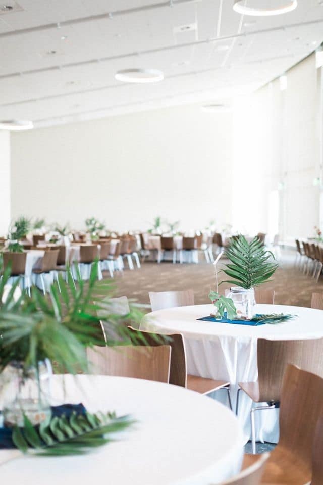 round tables with green palm centerpieces and brown chairs in elegant white ballroom